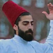 Tänzer in langem weißem Gewand vor städtischen Backsteinhäusern